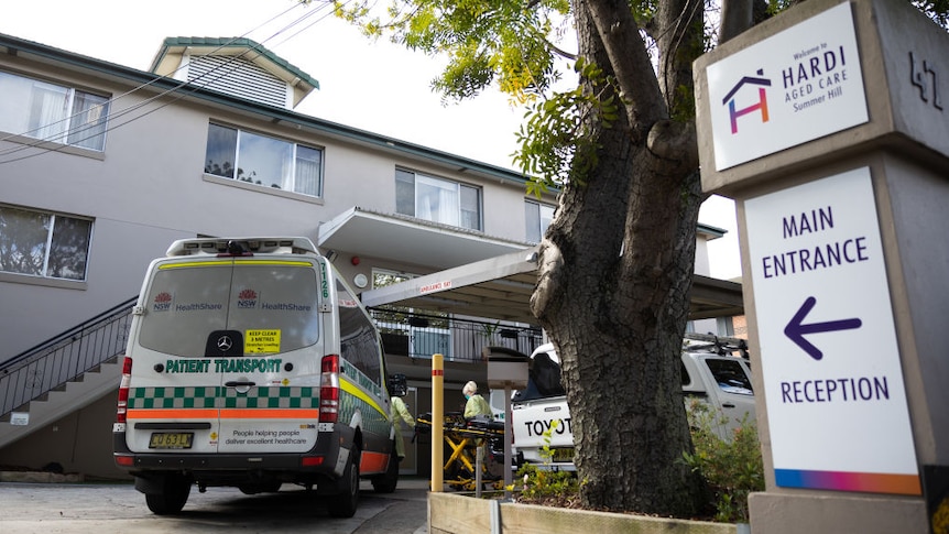 An ambulance parks outside Hardi Aged Care. Staff in PPE hold a gurney for transporting residents into the vehicle.