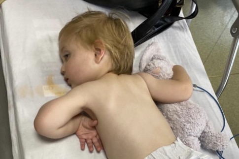 A sickly child lays on his stomach in a bed