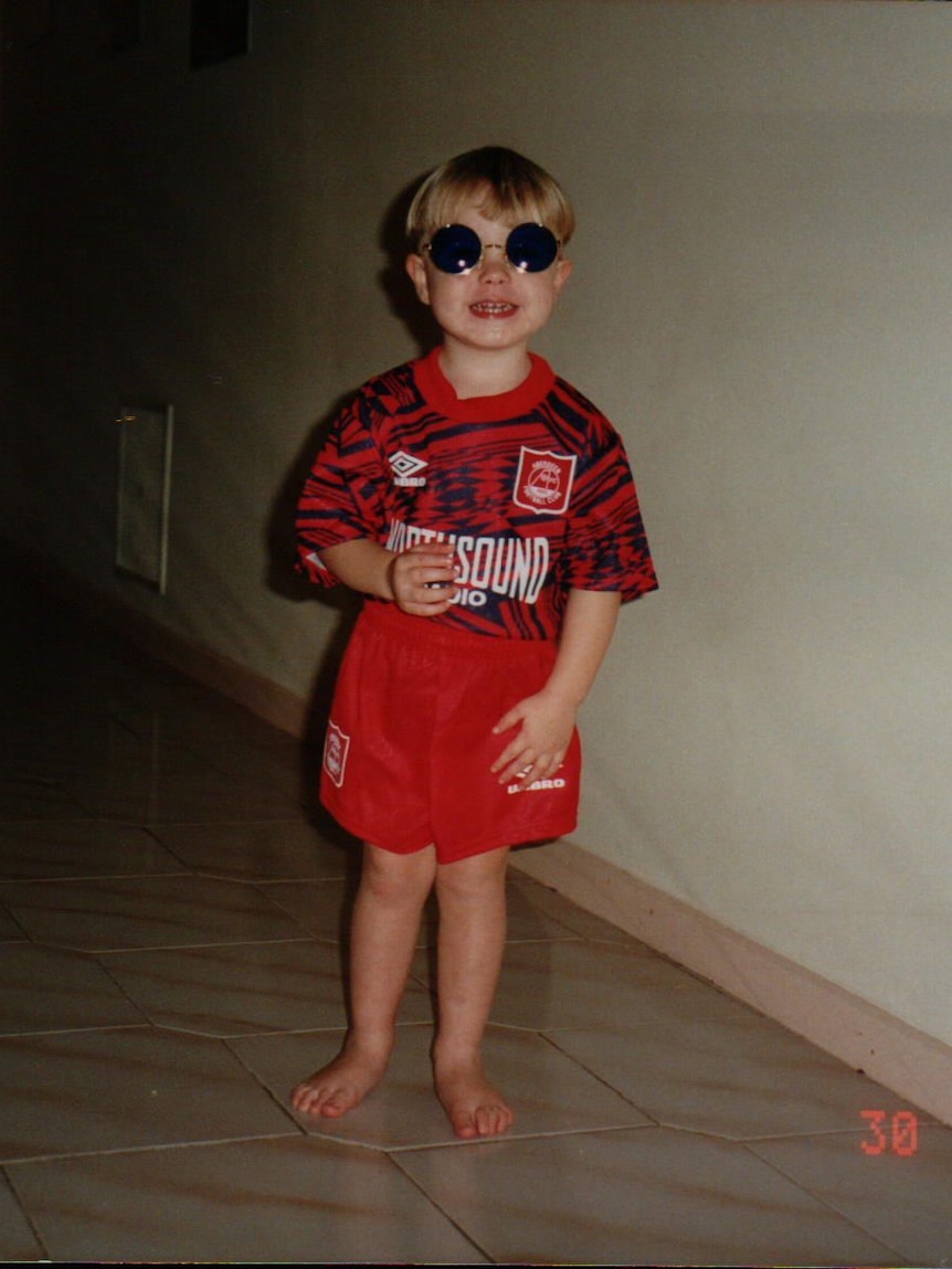 A young boy in sunglasses wears soccer clothes in red and white