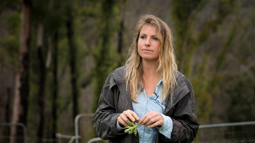 Srisa Heffernan looks into the distance, trees with green regrowth are in the background.