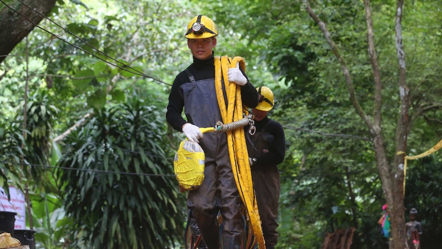 Rescuers carrying oxygen pipes walk out of a cave where a young soccer team and their coach are believed to be missing.