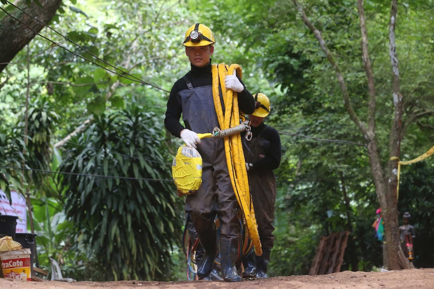 Rescuers carrying oxygen pipes walk out of a cave where a young soccer team and their coach are believed to be missing.