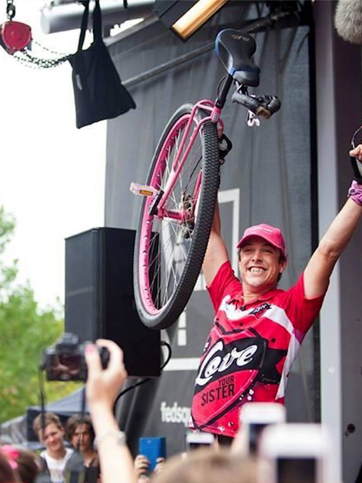 Man holding a unicycle, putting his fist in the air