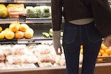 The back of a person standing in front of a refrigerated fresh produce section in a supermarket. 