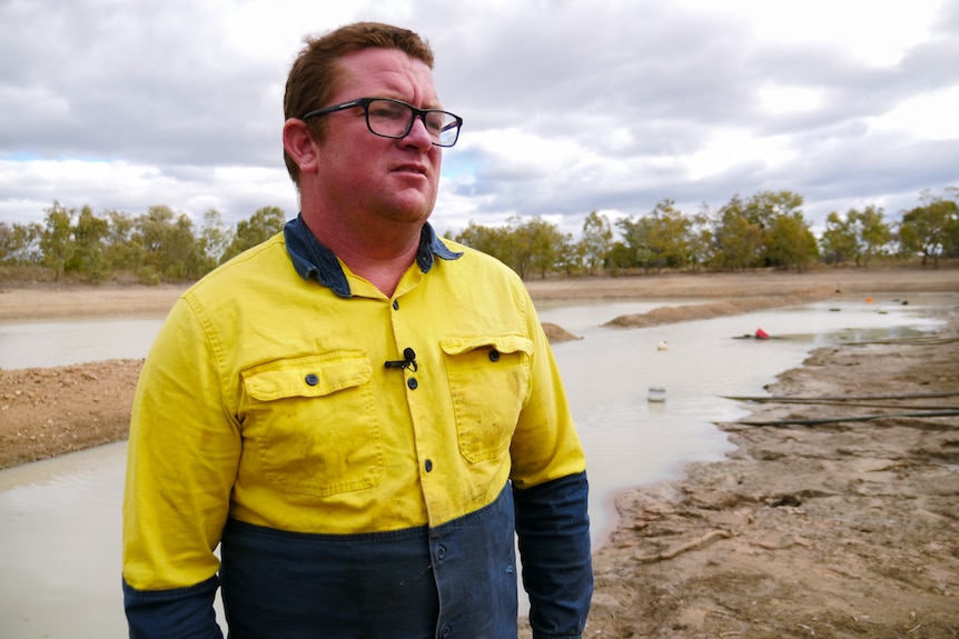 man stands in high vis top in front of near empty dam.