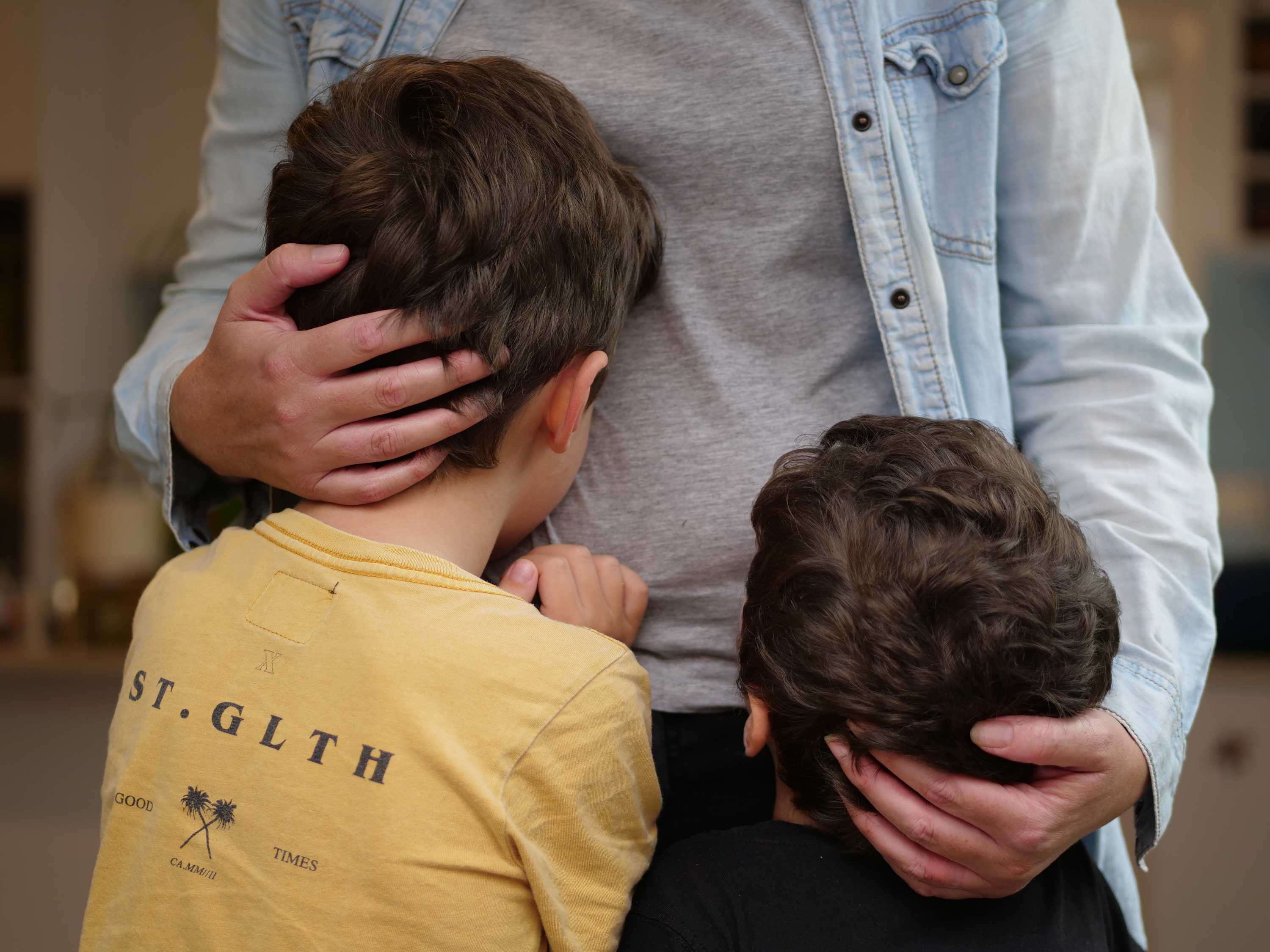 A mother hugs two young boys to her waist.