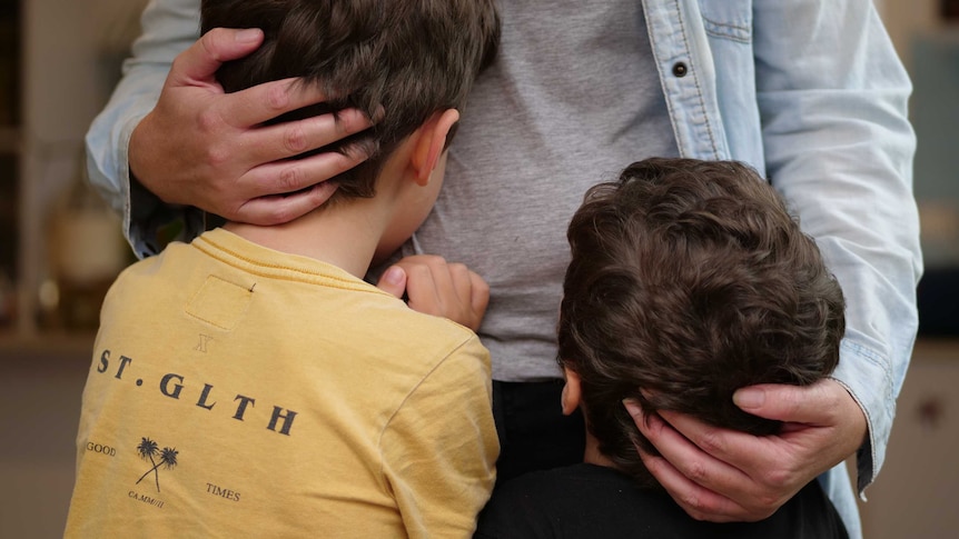 A mother hugs two young boys to her waist.