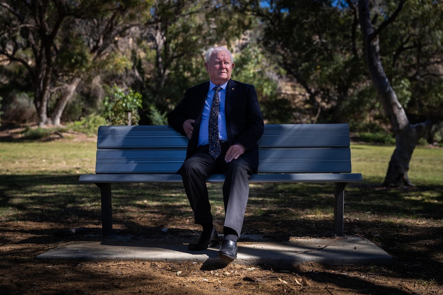 An older man sits on a park bench looking sad. 