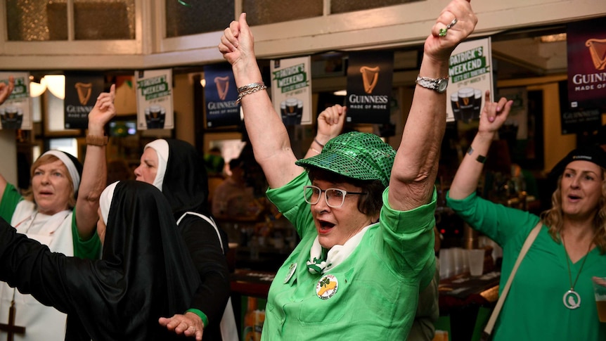 An older woman celebrates with arms in the air in green costume