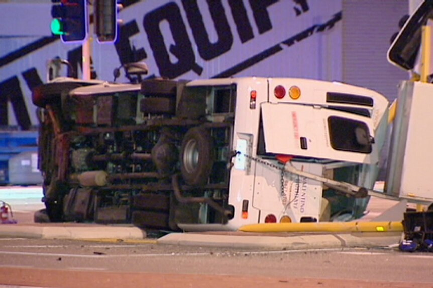 A bus lies on its side after colliding with a sedan at an intersection in Kewdale.