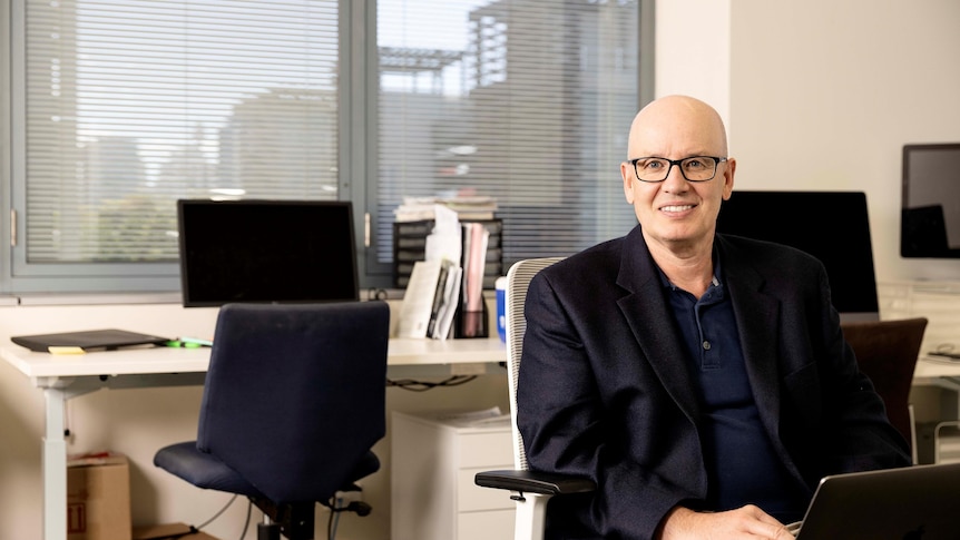 A man wearing glasses sitting at a desk in an office.