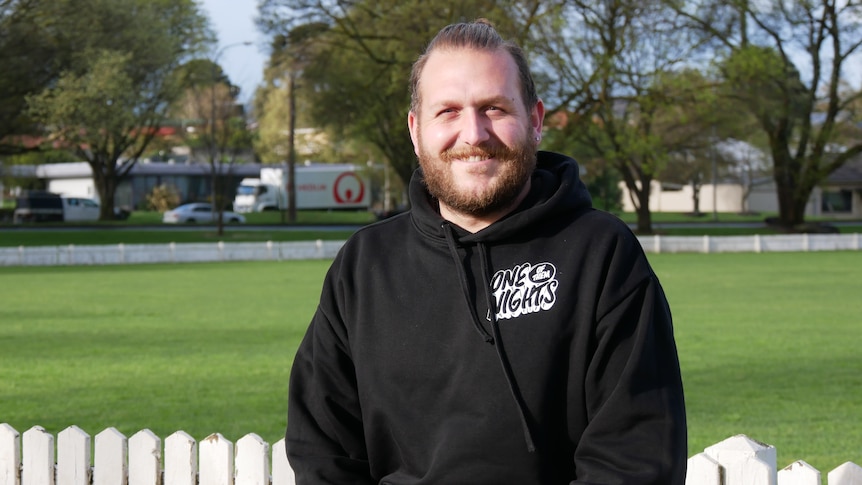 A man wearing a black jumper smiling at the camera. 