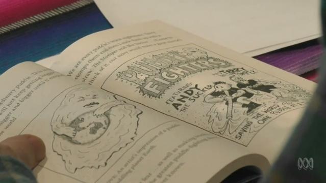 A hand holds open a novel with cartoon illustrations