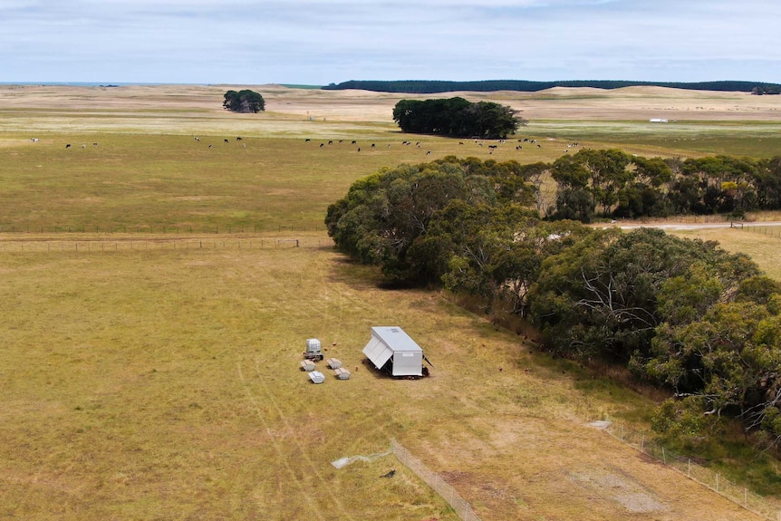 A drone shot shows a series of chicken caravans appearing small in a large paddock from up high in the sky.