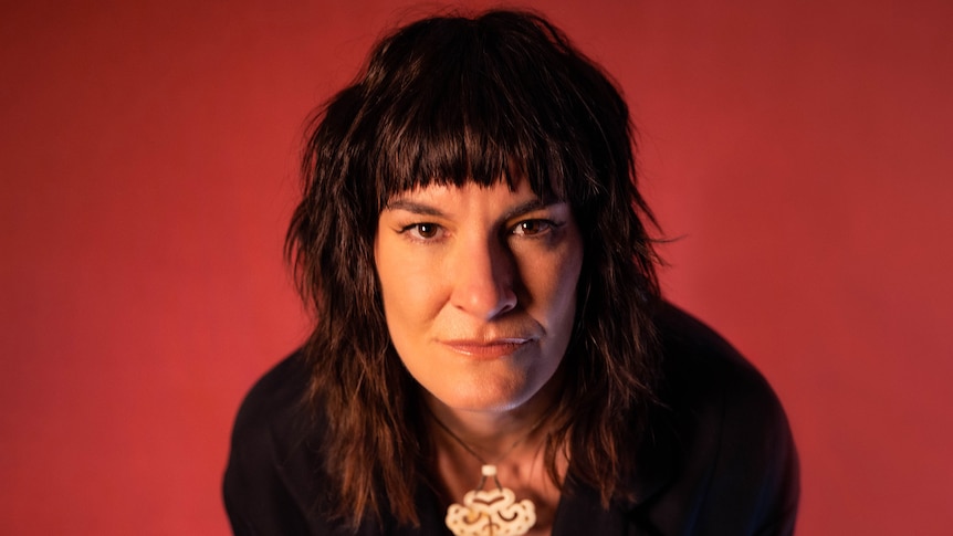 Jen Cloher is photographed looking at camera in front of a red background