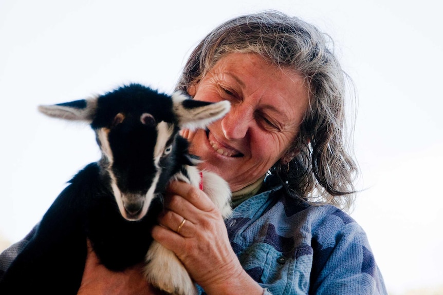 A woman with mid-length grey hair holding a small black and white goat.