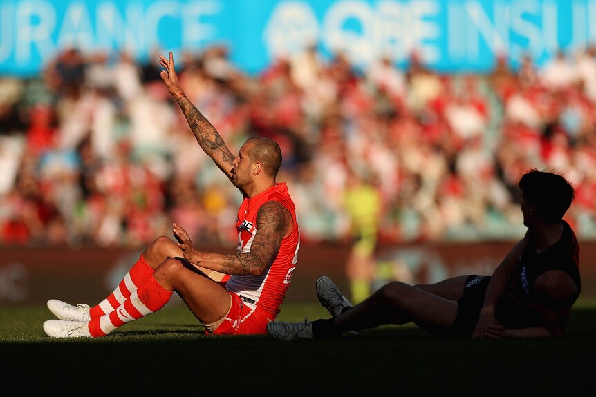 Lance Franklin points to the sky as he sits on the ground during Sydney's AFL win over GWS.