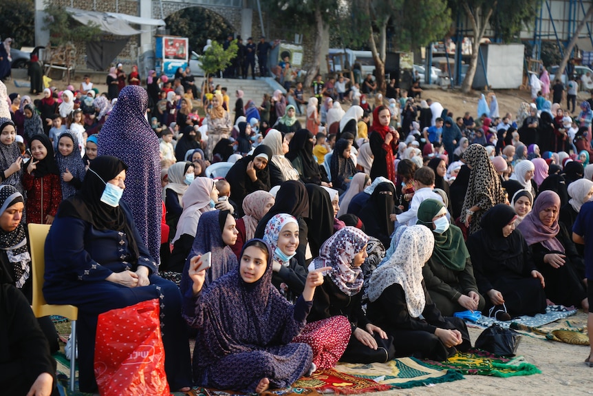 A group of female Muslims in hijabs sitting on top of their prayer mats outside the mosque