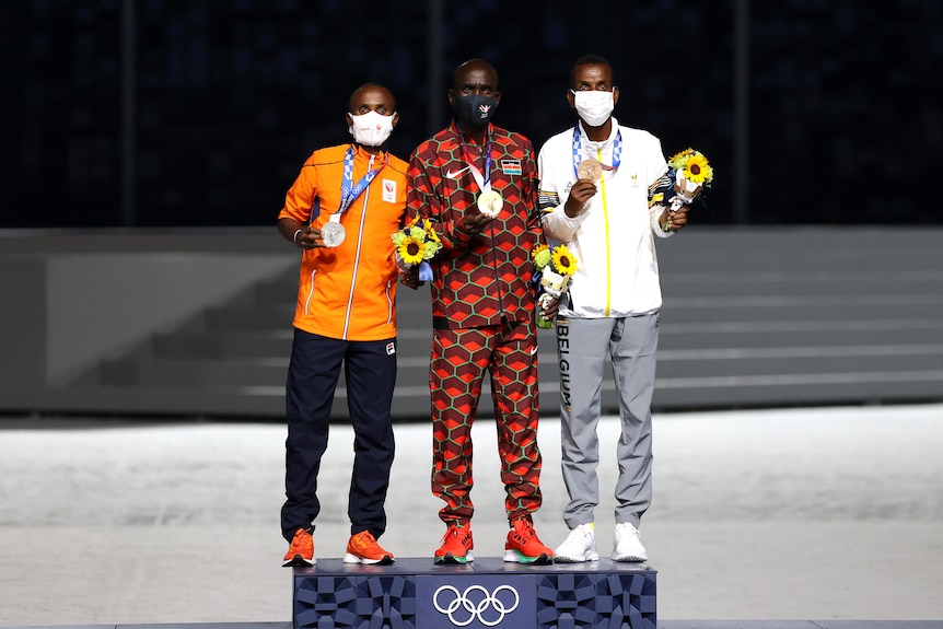 Men's marathon champion Eliud Kipchoge and the silver and bronze medallists stand on a podium 