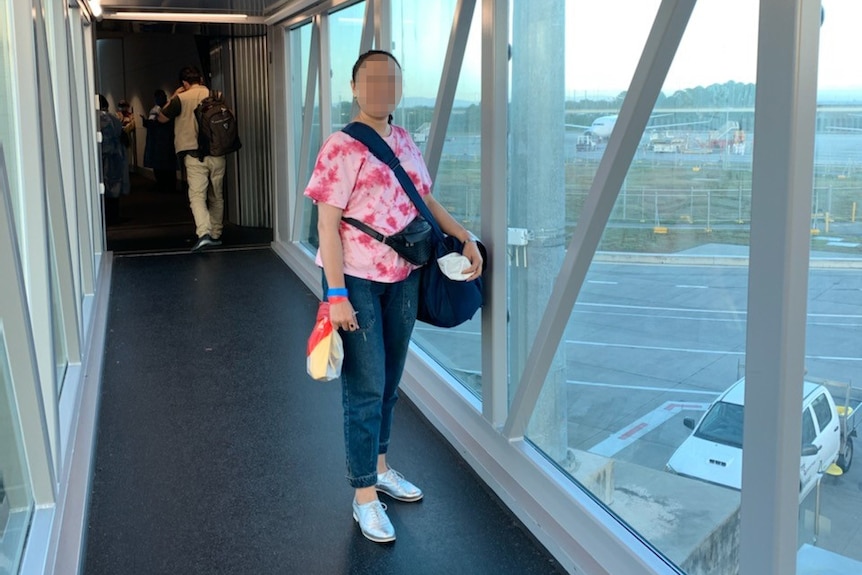 A woman wearing a pink shirt stands at an airport gate.