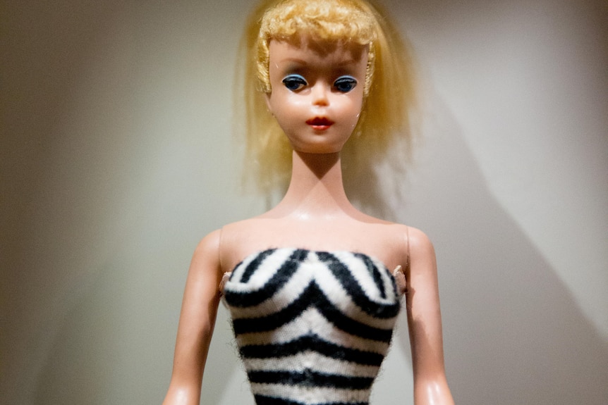 A close up of a doll with blonde hair and blue eye makeup wearing a zebra print swimsuit.
