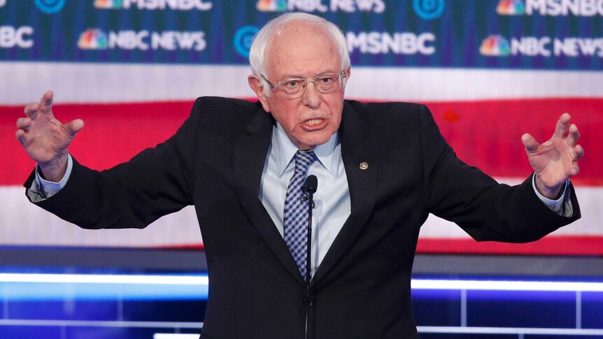 Bernie Sanders speaks with his arms wide open at a podium during a Democratic presidential primary debate in Las Vegas.