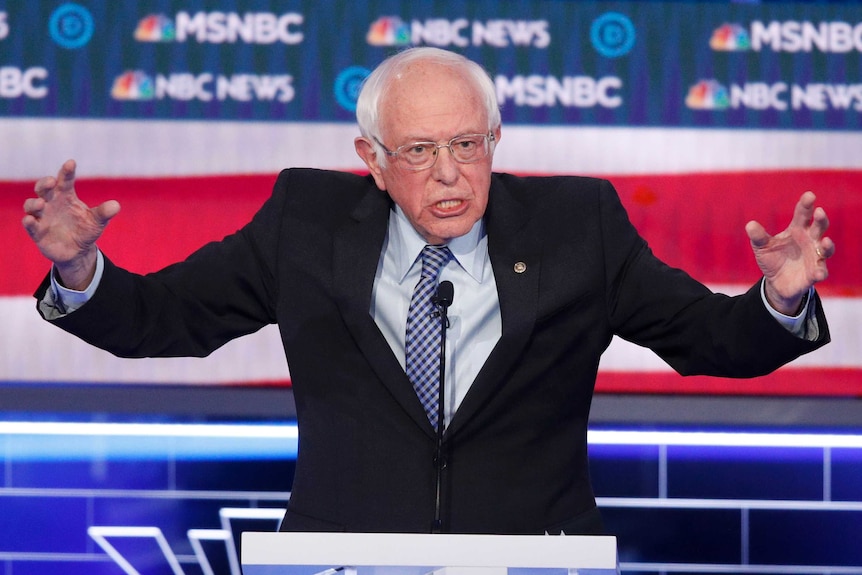 Bernie Sanders speaks with his arms wide open at a podium during a Democratic presidential primary debate in Las Vegas.