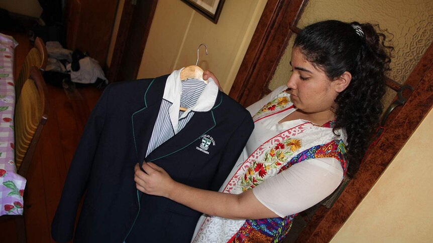 A teenager holds up a school dress and blazer
