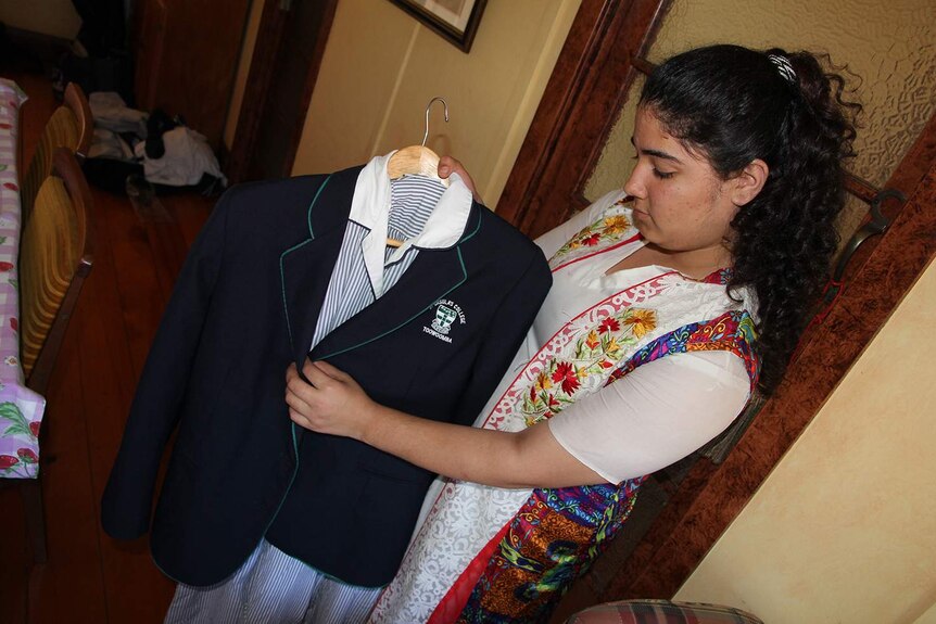 A teenager holds up a school dress and blazer
