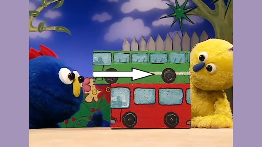 Blue and yellow puppet figures look at white arrow on buses