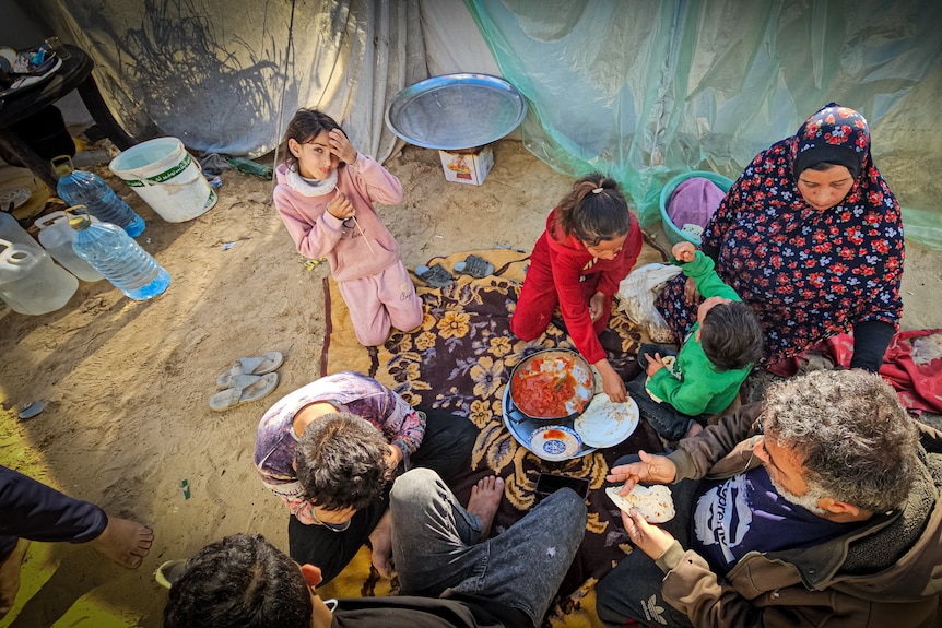 A family crouches around a pot, eating