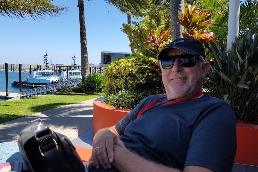 Steve Connelly sits with his camera and waterfront in the background