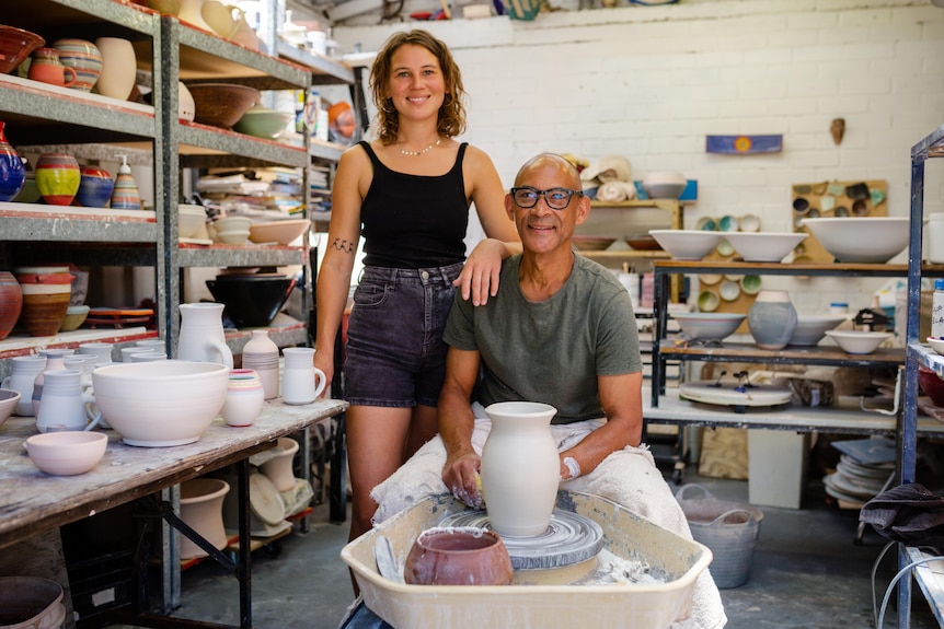 Shupiwe and Njalikwa stand next to the potter wheel in the pottery studio.