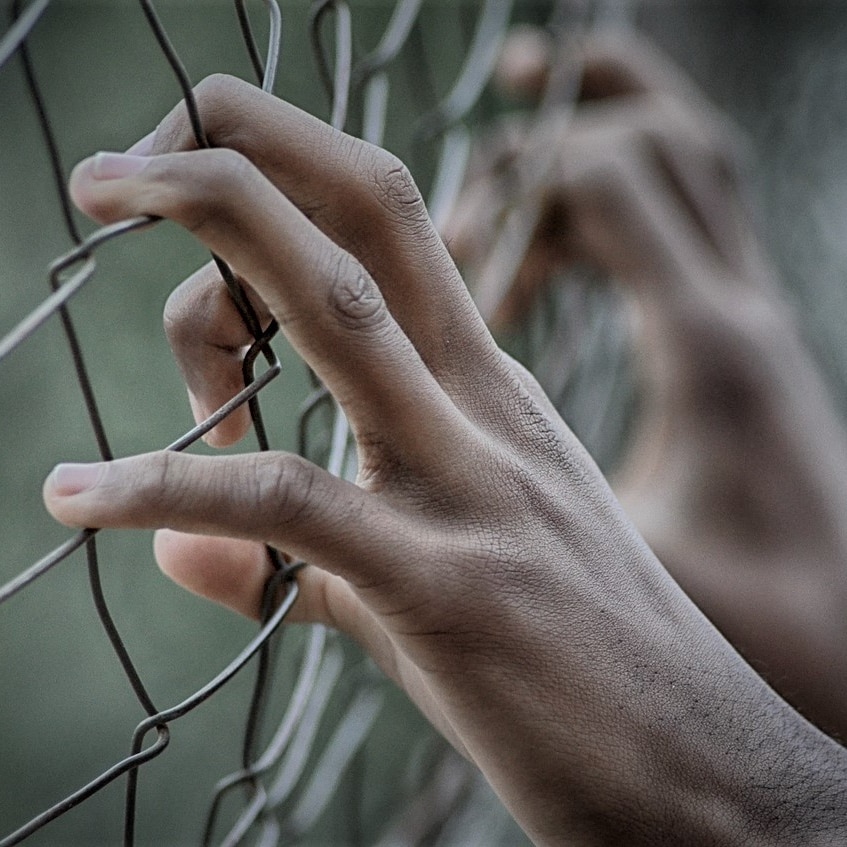 Hands grasping a cyclone wire fence.