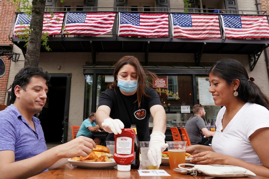 a waitress with a face mask serves diners at a restaurant in Alexandria, Virginia