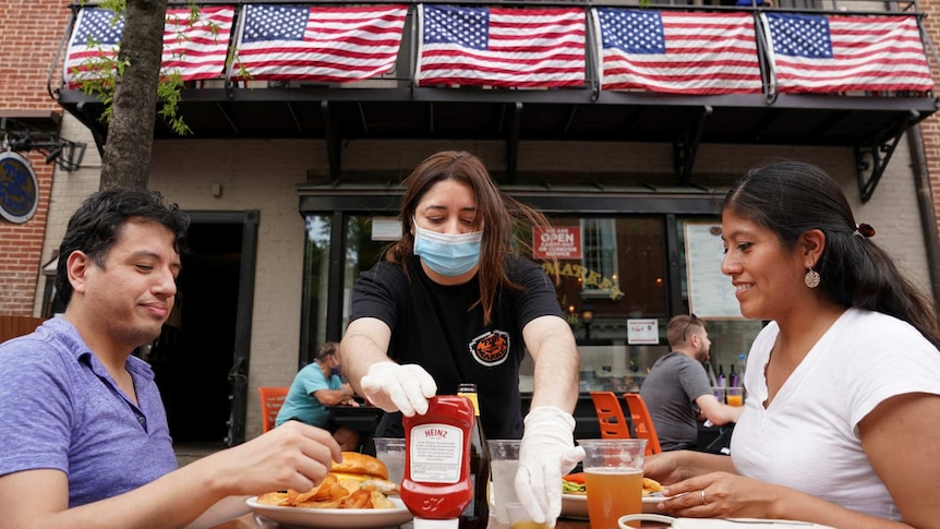 a waitress with a face mask serves diners at a restaurant in Alexandria, Virginia