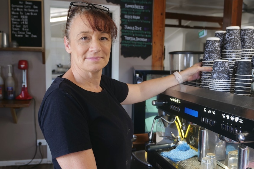 Kris Hargrave, dark shirt, redish brown hair, glasses on head, hand reaching for coffee cups on top of machine.