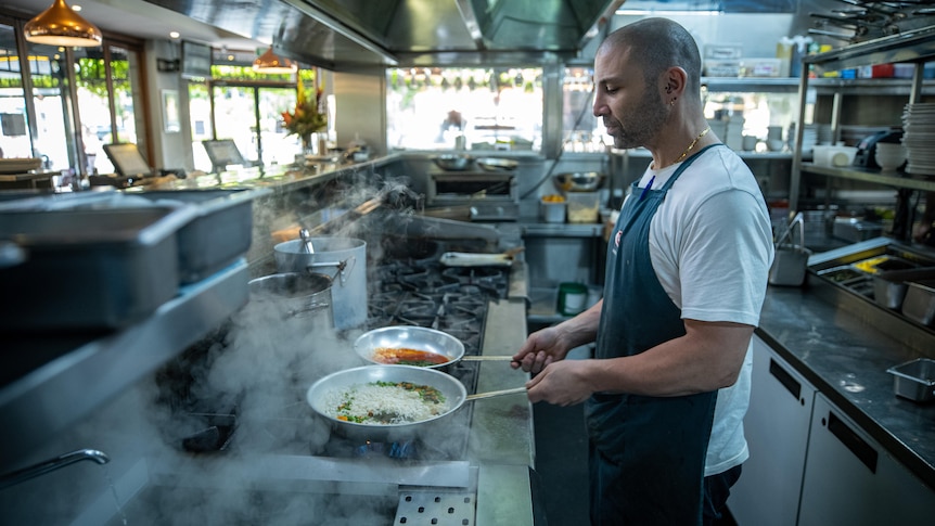 A man cooking holding two frypans