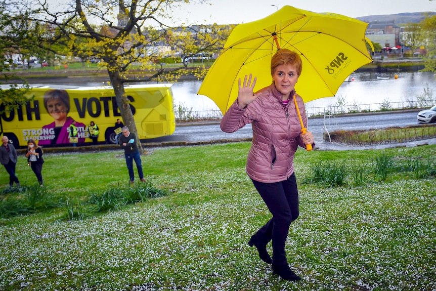 Nicola Sturgeon waves while holding a bright yellow umbrella