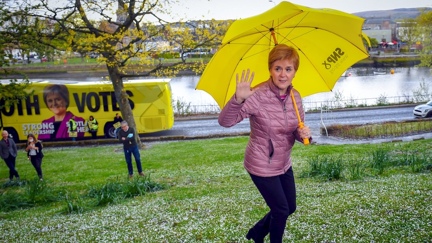 Nicola Sturgeon waves while holding a bright yellow umbrella