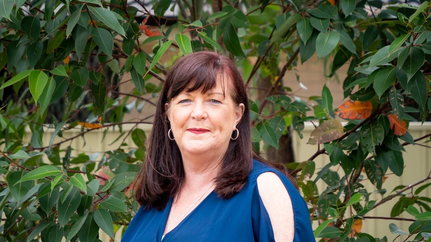 Kerrie Foord smiling, standing in front of a treet and wearing a blue top.