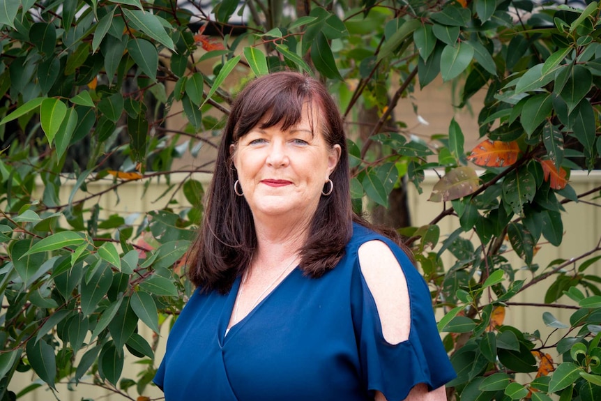 Kerrie Foord smiling, standing in front of a treet and wearing a blue top.