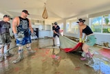 People dressed in gum boots pull at red carpet in a flooded room