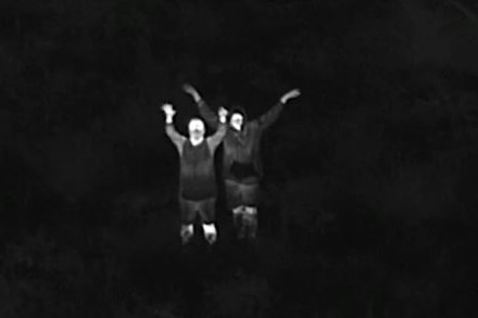 an infrared image of two white bodies with waving arms against a black background