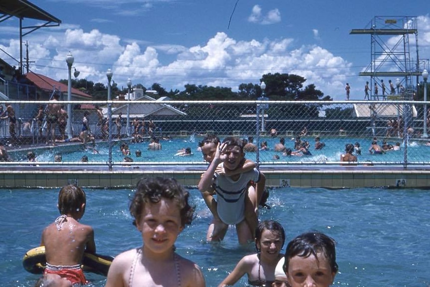 Kids play in a large public swimming pool.
