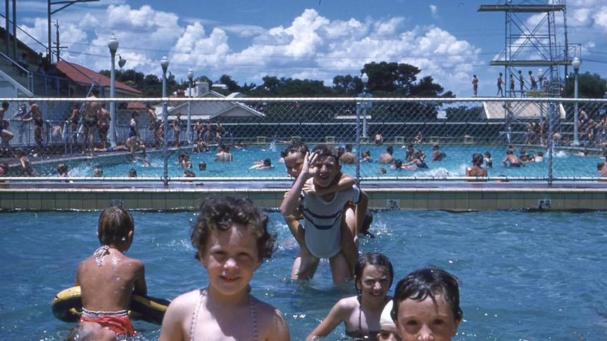 Kids play in a large public swimming pool.