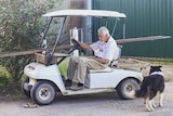Bob Gosbell sitting at a slumped angle behind the wheel with timber sticking out from one end of the golf cart to the other.