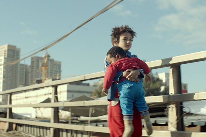 Colour photo of Zain Al Rafeea carrying Boluwatife Treasure Bankole along road in 2018 film Capharnaüm.