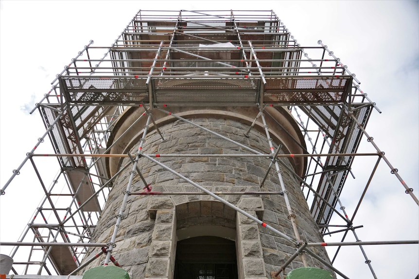 A shot of a lighthouse tower covered in scaffolding.