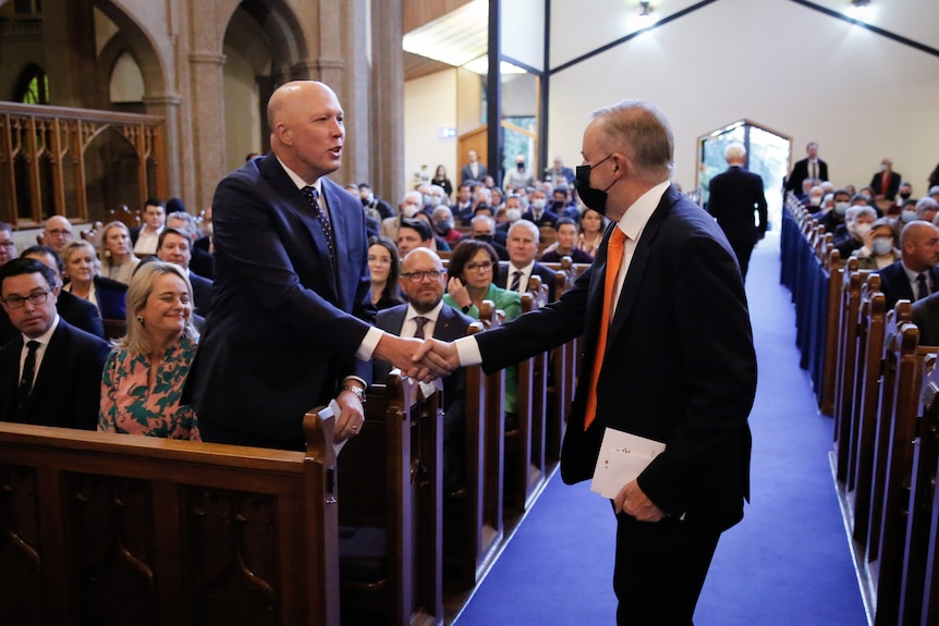 Albanese reaches out to shake Dutton's hand, who is standing behind a wooden pew, while at a church.